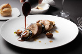 Une assiette blanche contient une préparation culinaire composée d'aliments coupés en morceaux et nappés d'une sauce foncée.