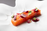 Une assiette blanche contient un morceau de saumon cru, garni de diverses herbes et légumes coupés en petites cercles.
