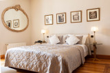 La chambre de la suite comprend un lit double avec du linge de maison clair, un mur avec des cadres et un miroir rond, et un sol en parquet.