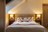 Cette chambre mansardée comprend un lit double avec une tête de lit en tissu, deux tables de chevet avec des lampes et du linge de maison clair, le tout dans des tons doux et naturels.