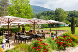 Cette terrasse en plein air comprend plusieurs tables et chaises disposées sous de grands parasols, avec une vue sur le parc thermal d'Uriage.